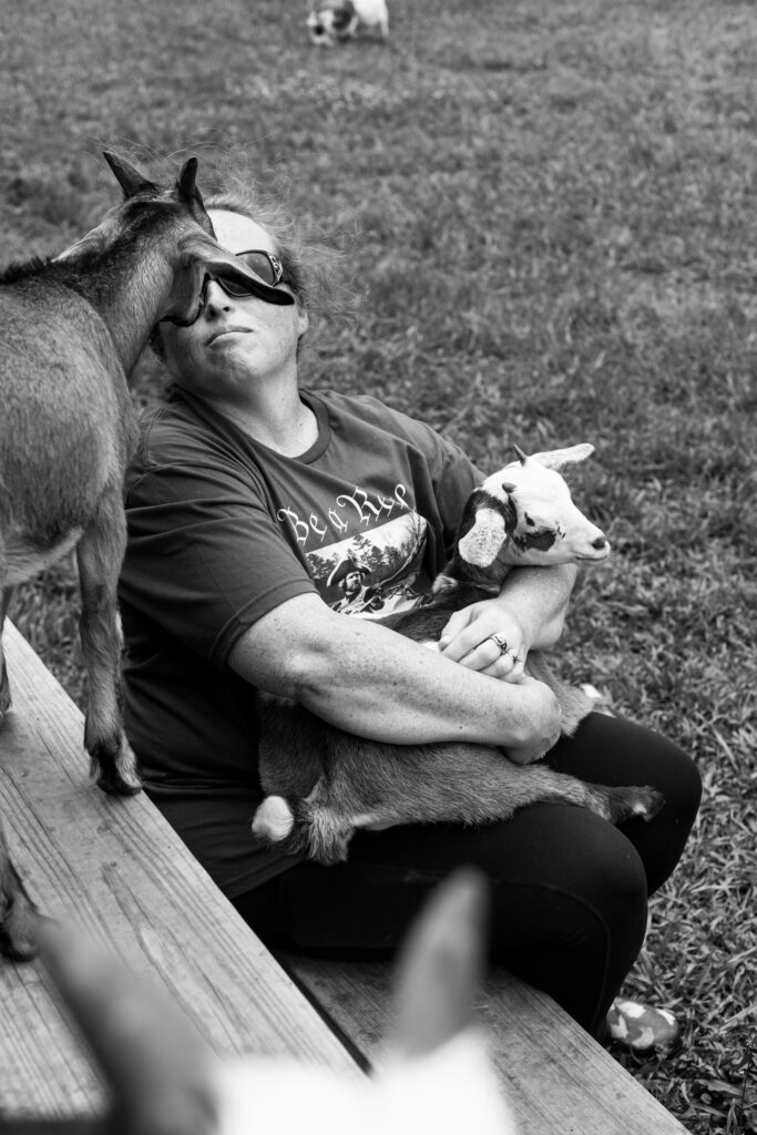 Jennifer Reed holds 1 goat as another leans over her.